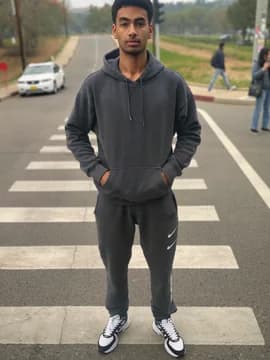 A young man at a crossing in a dark hoodie and joggers